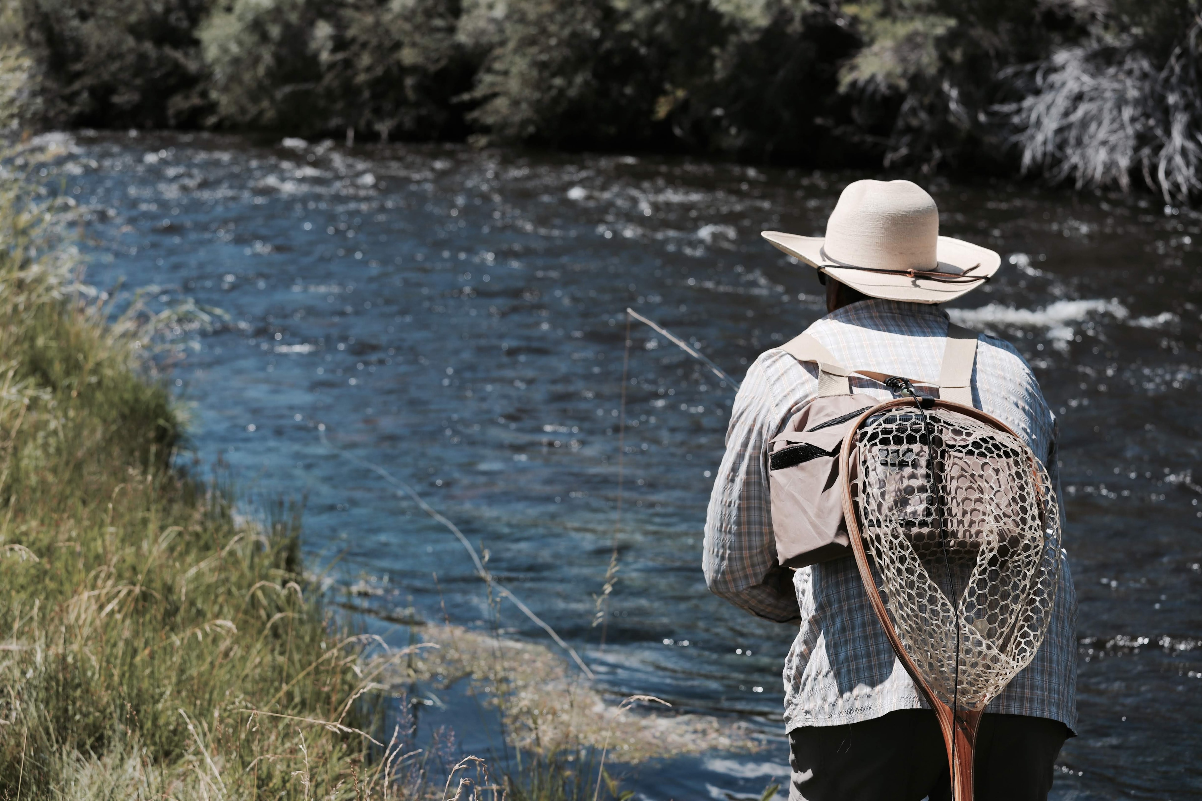 Classic rainbow trout cradled in a wooden net, vivid pink lateral stripe, red plaid sleeve